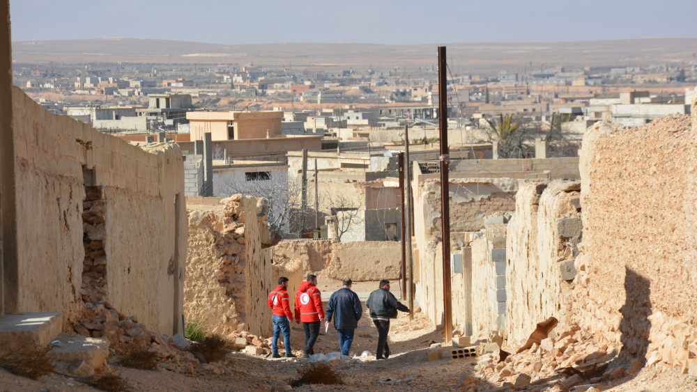 A group of four Red Cross workers walking through a street in a Syrian town.
