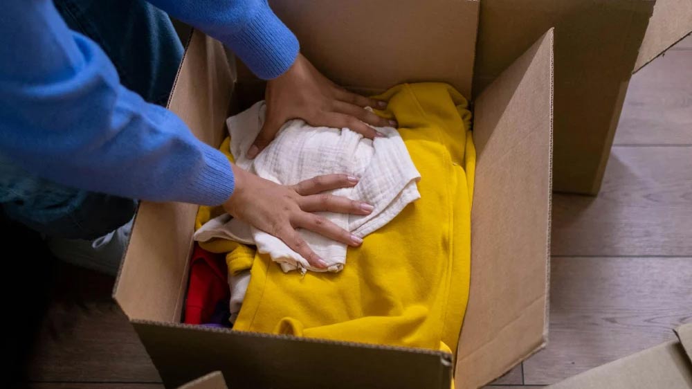 Hands packing a cardboard box with blankets and clothing